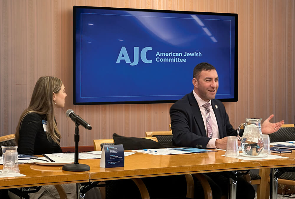 LCW student government president Talya Stauber, talking to NYC Councilman Eric Dinowitz at a table with AJC logo in the background 